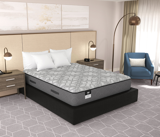 A modern bedroom with a low platform bed, beige padded headboard, two nightstands with lamps, a blue armchair by a window, an arched floor lamp, and a geometric gray carpet.